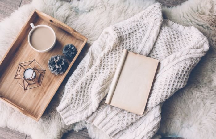 A cardigan, book and a tray with a candle and cup of tea situated on a fur blanket