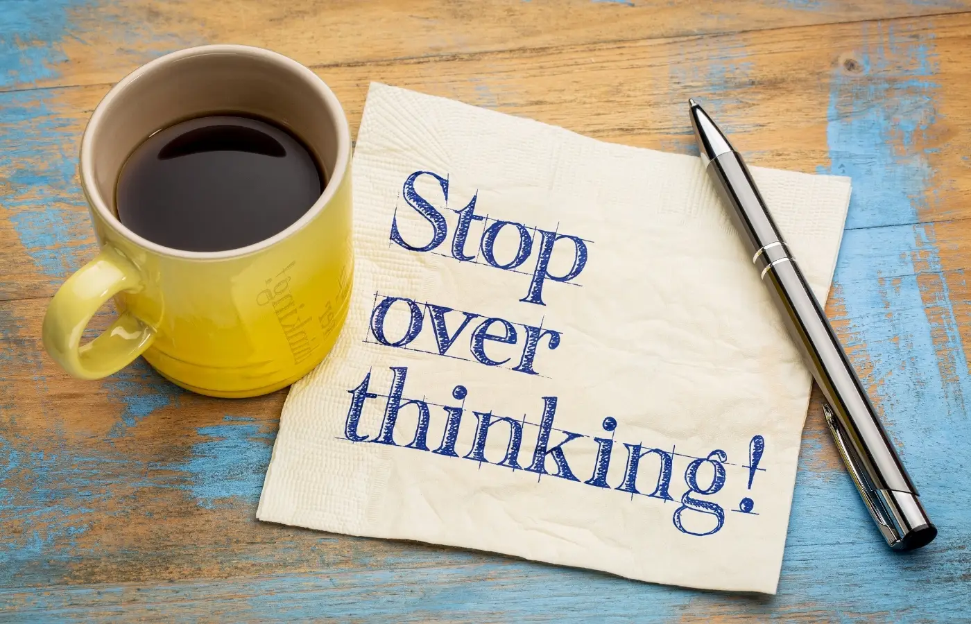 The text "How to stop overthinking" printed on a napkin sitting beneath a cup of coffee