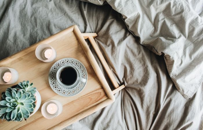 A tray with lit candles and a cup of coffee sitting in a bed.