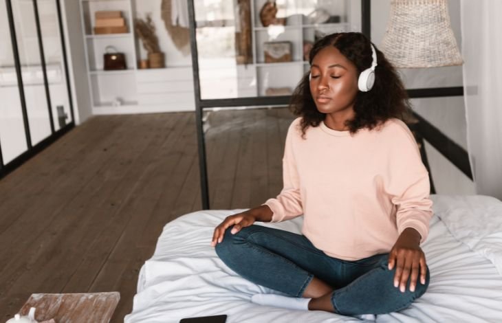 Woman with headphones sitting on a bed listening to one of the best apps for breathing exercises